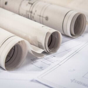 Vista en primer plano de un plano de ingeniería de una red eléctrica en tamaño pliego, siendo revisado por dos ingenieros de Estudios de Conexión para verificar la precisión de las conexiones y cotas impresas.