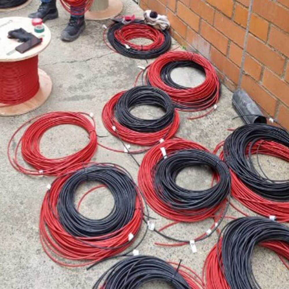 Instalación de cableado DC fotovoltaico de 6mm² de color rojo y negro, con marquillado en termoencogible claro, siendo tendido y peinado de forma ordenada por un técnico de Estudios de Conexión en un sistema de paneles solares en la azotea.
