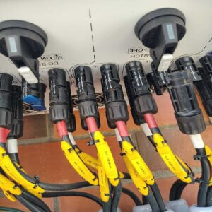 Un técnico de Estudios de Conexión utilizando una herramienta de ponchado calibrada para instalar un conector MC4 (positivo) en el extremo de un cable solar fotovoltaico, con el conector MC4 negativo y el cable preparado al lado.