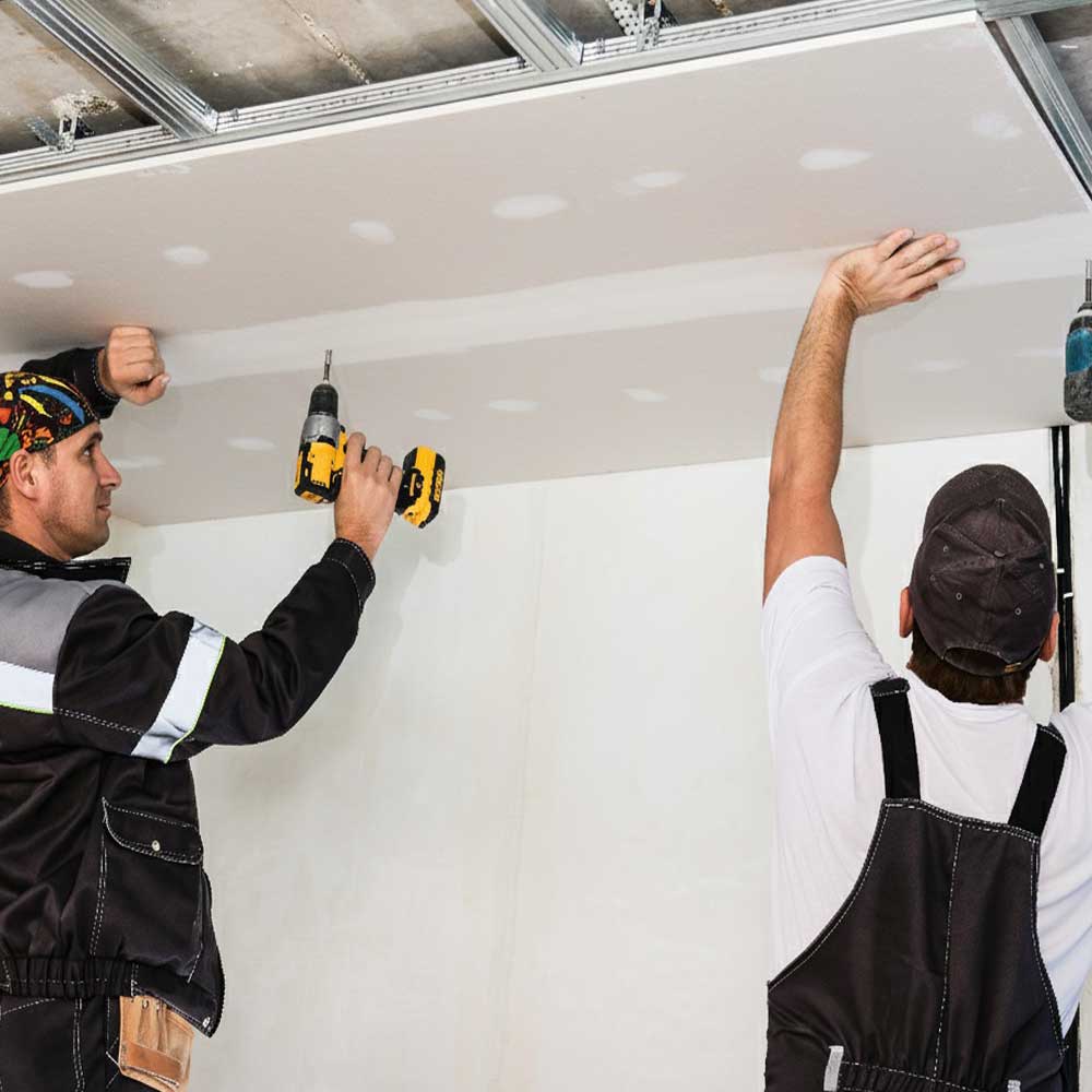 Dos trabajadores instalando una placa de drywall en un cielorraso. Se observa la estructura metálica de soporte y los técnicos utilizando taladros atornilladores para fijar las placas, ilustrando el proceso de instalación profesional de drywall modular.